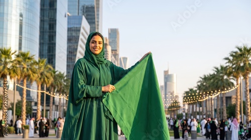 Saudi woman in green abaya proudly displaying large national flag outdoors during event   