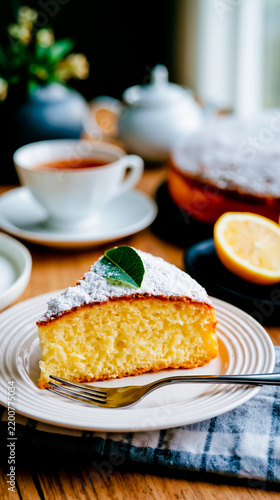 A slice of yellow cake with powdered sugar and a green leaf on a white plate