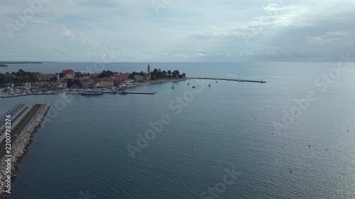 High distant drone shot showing the historic peninsula of Novigrad, harbor breakwater piers, marina basin, and expansive open Adriatic sea under a soft sky in Istria