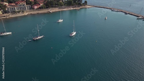 Elevated drone shot over calm turquoise harbor waters with anchored luxury sailboats, stone breakwater, and historic town waterfront of Novigrad Istria