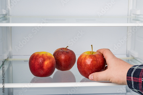 Hand picking fresh red apple from group in fridge