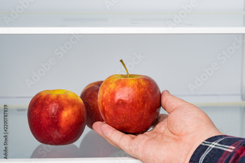 Hand picking fresh red apple from group in fridge