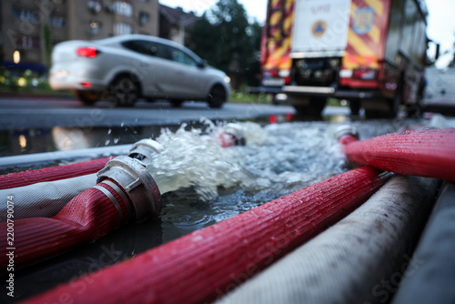 Water coming out of high-pressure red and white fire hoses along a city street during emergency flooding operations