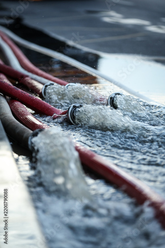 Water coming out of high-pressure red and white fire hoses along a city street during emergency flooding operations