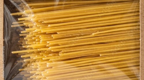 Uncooked spaghetti pasta packaged inside a brown cardboard box with a transparent plastic viewing window against bright studio background.