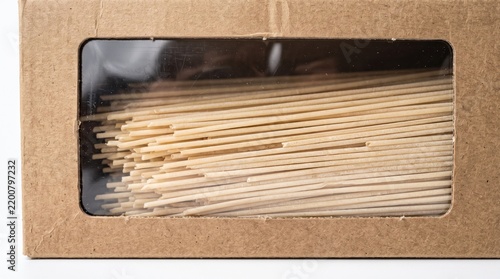 Uncooked spaghetti pasta packaged inside a brown cardboard box with a transparent plastic viewing window against bright studio background.
