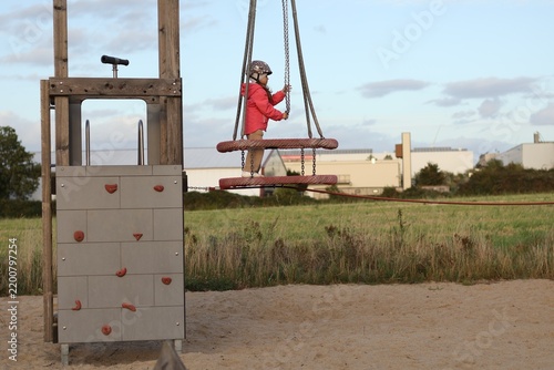 фотографія Young girl playing on a playground rope swing structure outdoors at sunset