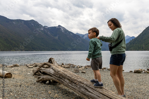Mother And Son Exploring Driftwood On Rocky Shore At Chilliwack Lake, BC Canada With Mountains