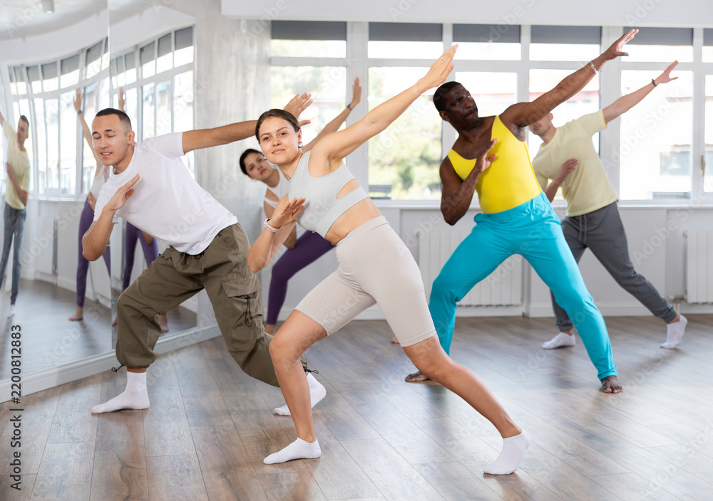 Fototapeta premium Happy emotional sporty young female dancer rehearsing popping techniques during group workout in modern street dance studio