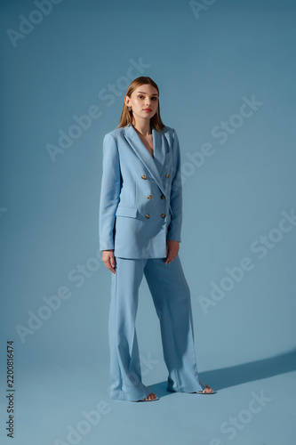 Beautiful fashionable woman wearing trendy blue color trouser suit, pantsuit, posing on blue background. Full-length studio fashion portrait. Copy, empty space for text