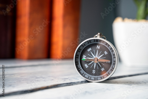 A compass lying on a table against a background of books