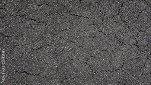 Close-up of cracked asphalt road surface showing textured dark pavement and granular aggregate