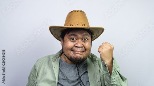 Foto Featuring an awkward yet determined smile, one young Asian male poses against plain light background wearing green casual apparel plus western headwear