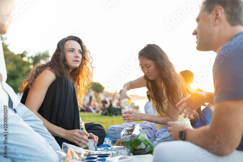 People gather on a grassy area for a social event during sunset, enjoying snacks and drinks