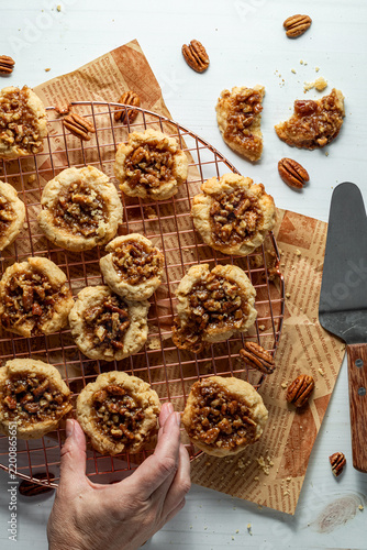 A top down view of a hand taking a pecan pie cookie from a cooling rack of many.