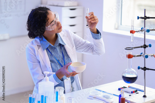 Pretty young African-American female chemist with mortar and test tube workin...