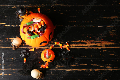Decorative pumpkins with different sweet candies and skulls on black wooden b...