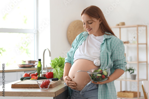 Young pregnant woman with vegetable salad in kitchen