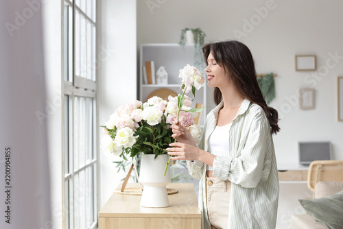 Young woman with bouquet of peony flowers on commode at home