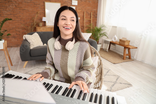 Beautiful young woman playing synthesizer at home