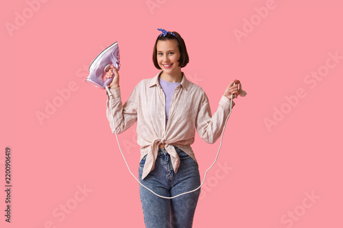 Smiling young woman with iron on pink background