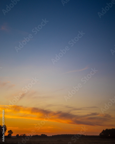 Vibrant twilight sky with orange cirrus clouds over rural landscape silhouette