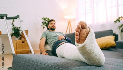 Young man with a broken leg in a cast resting on a couch at home