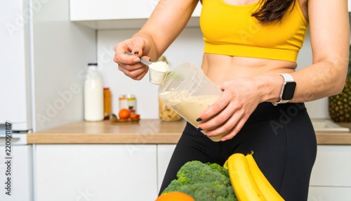 Fit Woman Preparing Protein Shake With Powder Scoop in Modern Kitchen