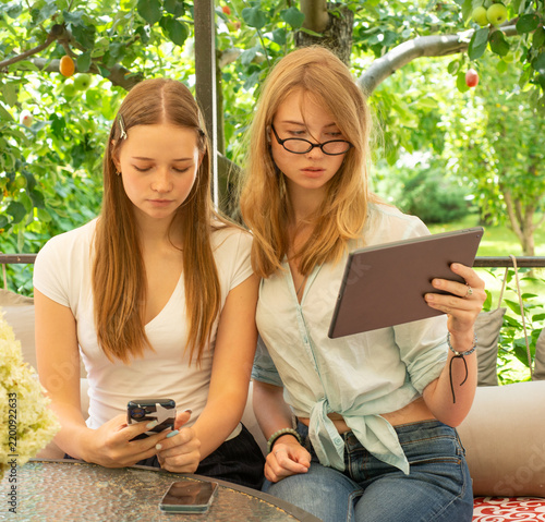 Two young female students are chatting in a gazebo, using a tablet and a smartphone.