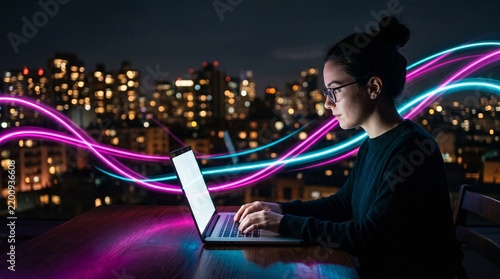 Focused young woman works on laptop computer with colorful neon light trails at night. Female freelancer uses digital tech in modern urban office. Creative pro programmer types on keyboard amidst