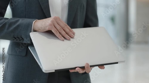 Professional businesswoman standing in corporate office holding laptop computer