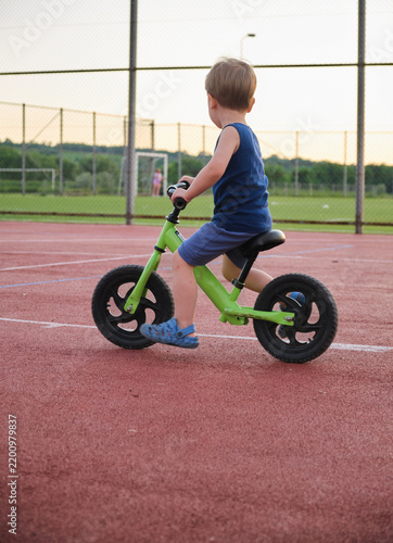 Child rides balance bike on outdoor playground surface during evening