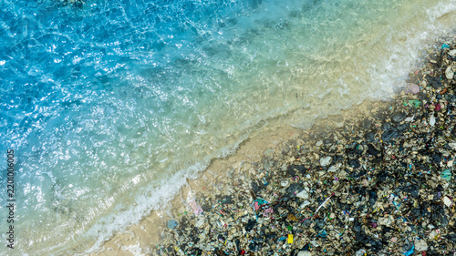 Top view of a beautiful turquoise beach polluted with a large pile of plastic waste and garbage; concept of ocean pollution, environmental crisis, and the impact on marine ecosystems.	