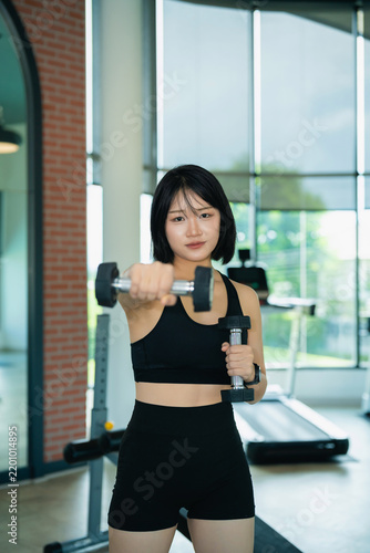 Fotografie Young Asian woman in black sportswear exercising with dumbbell in modern gym for