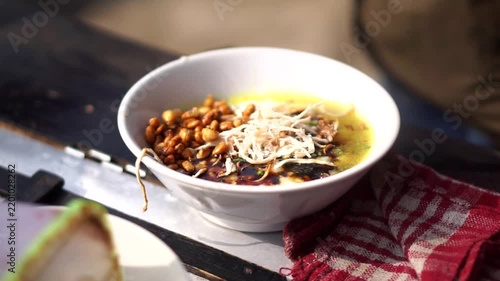 A bowl of traditional Indonesian chicken porridge served in a white ceramic bowl with shredded meat, fried peanuts, and savory yellow broth.