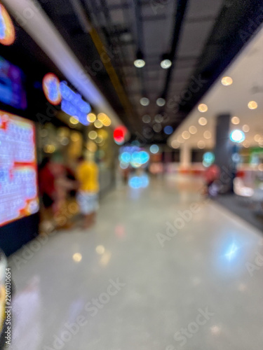 Blurred image of people walking down a wide, well-lit corridor in a modern shopping mall or large retail center, with colorful bokeh lights.