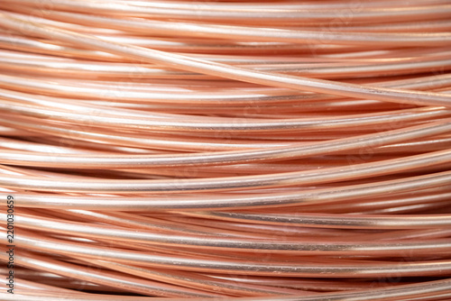 Close-up of coiled copper wires, showcasing their shiny surface and intricate overlapping pattern, captured in warm lighting.