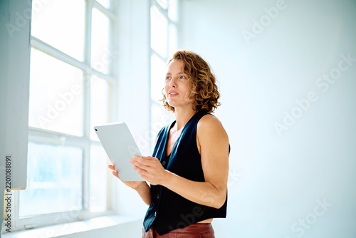 Fotografie Woman holding a digital tablet in a bright modern office, planning strategies an