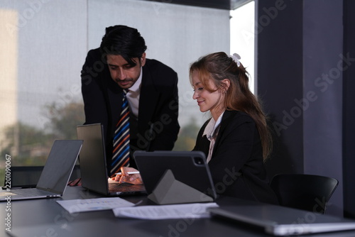 Fotografía Seated strawberry blonde professional lifts her stylus toward the tablet as her supervisor leans in close, both concentrating at the paper strewn window desk in a bright modern coworking