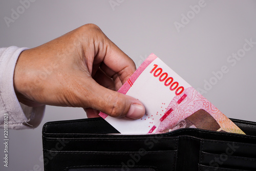 Konstfotografi A close-up shot of a person's hand pulling out or inserting a single Indonesian one-hundred-thousand rupiah bill from a black leather wallet against a plain grey background