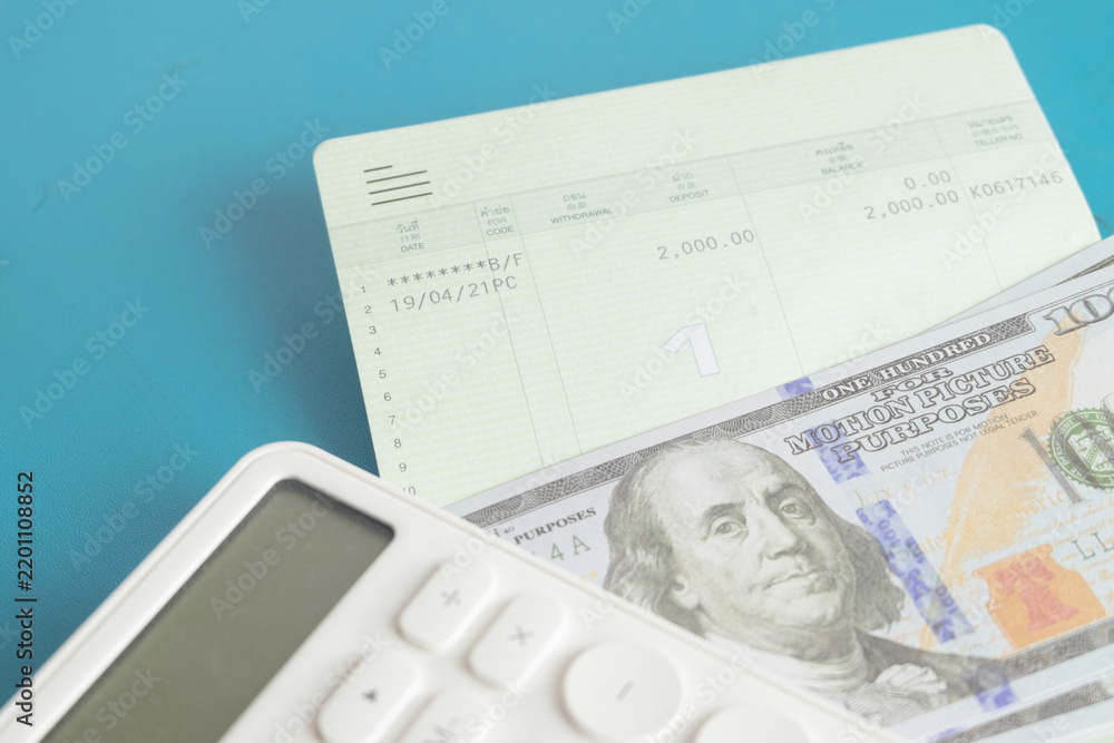 Obraz premium Close up of a white calculator, bank savings passbook and US dollar bills on a blue background. Concept of personal finance, saving money, budget calculation, accounting and wealth management.