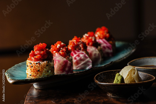 Bild auf Leinwand Gourmet spicy tuna sushi rolls garnished with red tobiko caviar and sesame seeds on a teal plate with vasabi and ginger