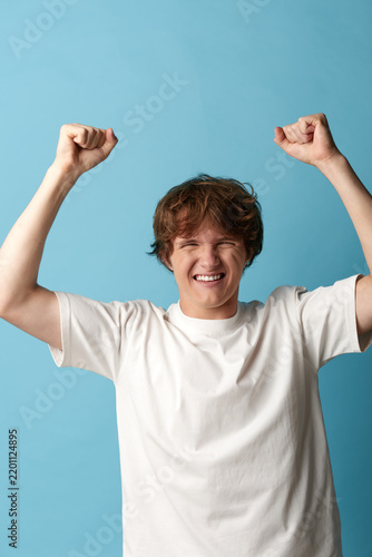 Foto Cheerful young man in white t-shirt celebrating with raised fists and happy laugh
