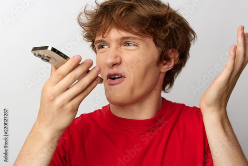 Obraz na płótnie An annoyed young man makes an exasperated argument gesture while holding a phone