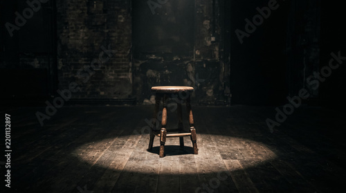 Wooden stool centered in a dark room illuminated by a single spotlight