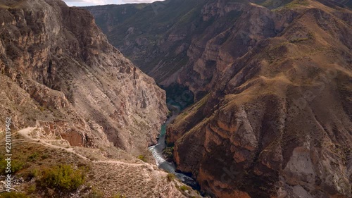 Rugged canyon overlook with steep layered cliffs, winding river, distant ridgelines, and cloud filled sky above, showing static natural terrain with dramatic travel mood