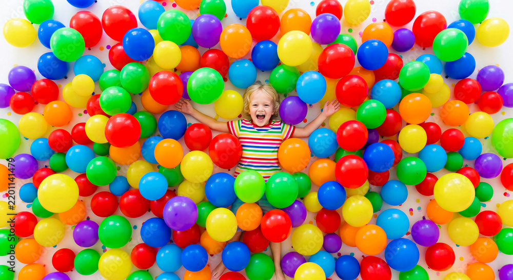 Obraz premium Happy young child lying in a pool of colorful balloons, joyful expression, bright festive atmosphere. Celebration, birthday, childhood joy, party concept.