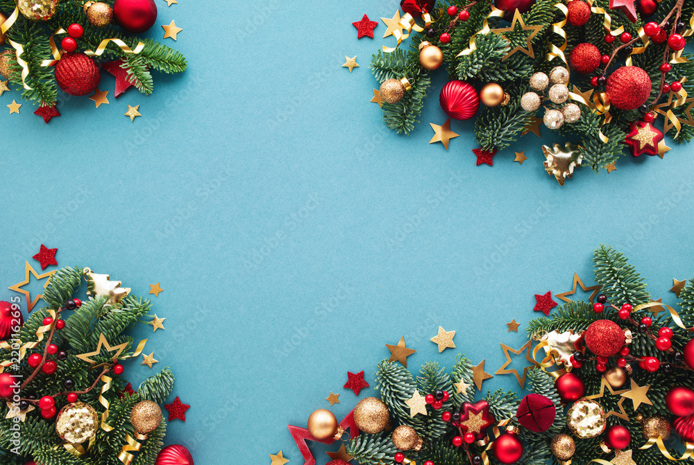 Obraz premium Christmas and New Year celebration arrangement on blue background with green fir branches, shiny decorations, confetti stars ornaments top view.