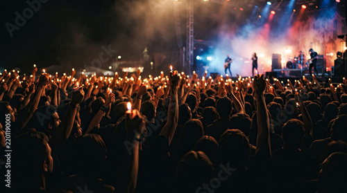 Passionate concert crowd holding glowing lighters and candles up high during an emotional rock band live show.