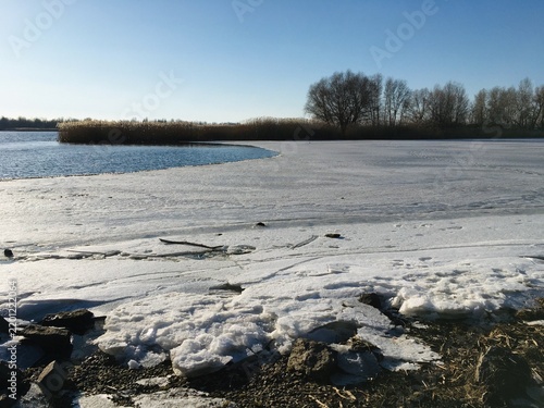 Foto River shore with melting snow on broken ice and freed waters flowing in calm tid